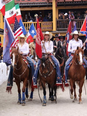 Eine Gruppe von Menschen reitet auf Pferden durch die Straßen von Pullman City Western town im Bayerischen Wald.